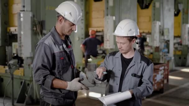 Dos ingenieros están inspeccionando la muestra del detalle del metal en un taller, un hombre está tocando la superficie — Vídeo de stock