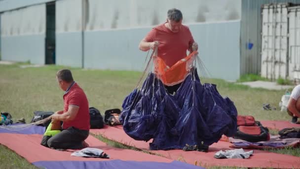 Dva dospělí muži jsou kontrola zvony paraglidisty na otevřeném prostoru v létě den, ležící zařízení na trávě — Stock video