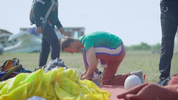 Paracaidistas se están preparando para el vuelo en tierra, el hombre está comprobando el equipo en el día de verano, grupo de deportistas — Vídeos de Stock
