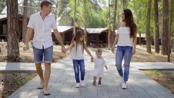 Familia feliz está caminando en la zona del complejo en el bosque en el día de verano, tomados de la mano de sus hijos pequeños — Vídeos de Stock