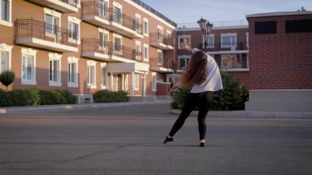 Giovane interprete di danza femminile sta ballando in un cortile di fronte a moderne case di soggiorno in una città in serata estiva — Video Stock