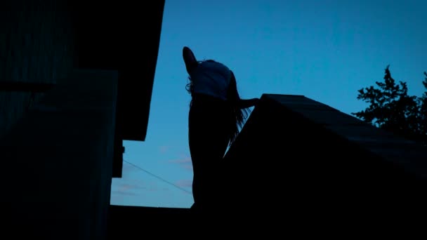 Jovem mulher sexual magro está dançando em um telhado de casa após o pôr do sol, vista na silhueta de seu corpo — Vídeo de Stock