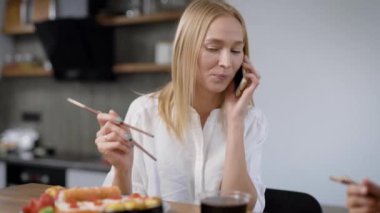 Sarışın genç kadın evinde, suşi ile akşam yemeği sırasında telefon üzerinde cevap o bir mobil baskı yapıyor