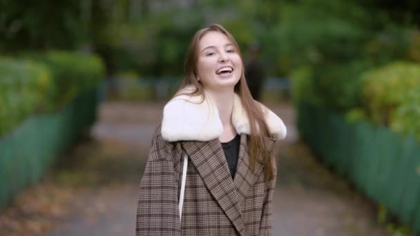 Solo bonita morena mujer está de pie en una calle en el callejón en el parque en el día de otoño, riendo y moviendo las manos — Vídeo de stock