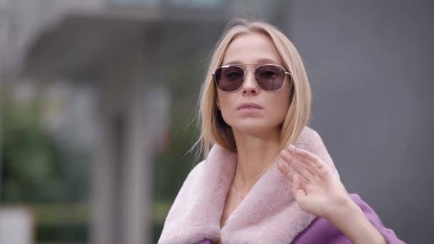 Mujer rubia adulta de moda está corrigiendo sus gafas de sol, de pie al aire libre en el día de otoño en la ciudad — Vídeo de stock