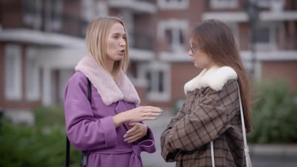 Två vackra kvinnor står i gården av levande byggnader i en stad under hösten och chattar, en vänner talar — Stockvideo