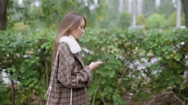 Mulher andando perto de arbustos e usando smartphone — Vídeo de Stock