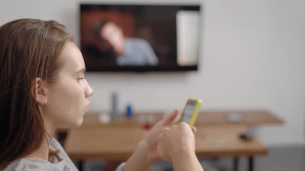 Jonge vrouw met behulp van smartphone in de buurt van de Tv op kamer — Stockvideo