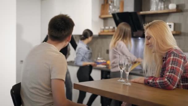 Cinco jóvenes están descansando en una pequeña fiesta en casa en vacaciones, la pareja está bebiendo vino y sus amigos están cocinando — Vídeos de Stock