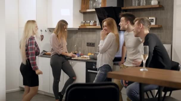 Радісна жінка і студенти чоловічої статі спілкуються на кухні під час домашньої вечірки, посміхаючись і сміючись — стокове відео