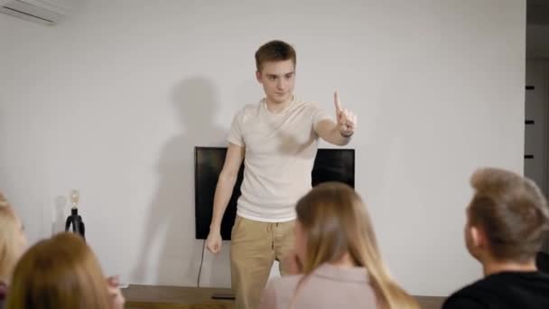 Group of young people are playing charades in apartment, funny man is showing images and other are guessing — Stock Video