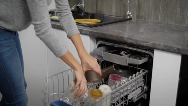 Женщина разгружает посудомоечную машину на кухне, кладет посуду в шкаф . — стоковое видео