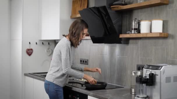Belle brunnete fille cuisine dîner dans la cuisine à la maison, friture sur une poêle . — Video