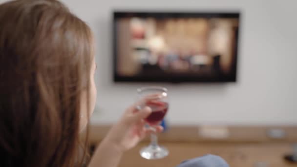 Zbliżeń, Dziewczyna, picie czerwonego wina podczas oglądania Tv show w salonie, spokojny czas sam w domu. — Wideo stockowe