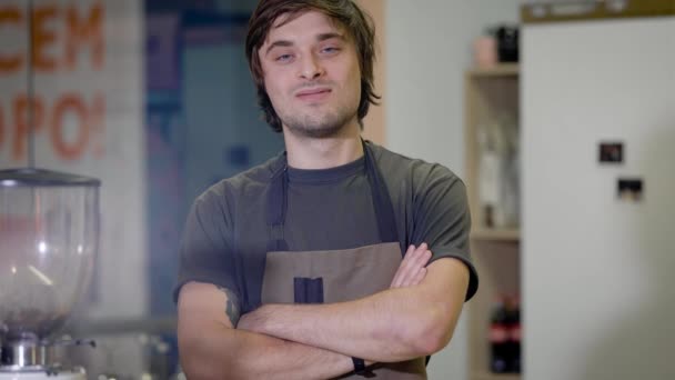 Drôle beau barista jeune homme pose pour un appareil photo dans un bar, croisant les mains et grimaçant plaisanterie — Video