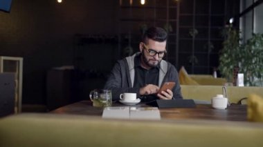 yakışıklı hipster adam Restoran gündüz, tablet önünde oturan Smartphone ekranında yazarak