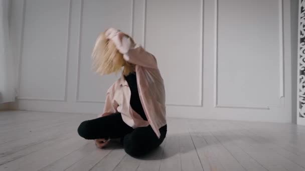当代女性舞蹈演员独自在舞厅训练, 坐在地板上, 腿向上移动 — 图库视频影像