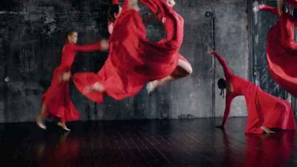 Jovens dançarinas de balé do sexo feminino estão dançando dança contemporânea em ensaio no salão escuro, vestidos vermelhos estão balançando — Vídeo de Stock