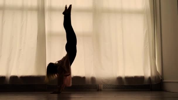 Femme mince danse dans une salle de répétition contre d'énormes fenêtres avec des rideaux, silhouette de figure — Video