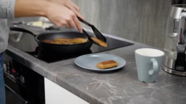 Genç dikkatli kadın krep tava alarak ve mutfak masasının üzerinde bir tabakta sabah zamanında koyarak