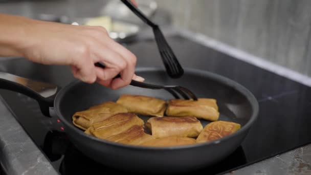 Женщина жарит блинчики с начинками на сковороде в домашней электроплите, крупным планом рук — стоковое видео