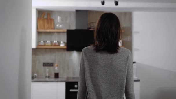 Young woman is walking in her flat in night time, moving on kitchen and taking glass with water — Stock Video