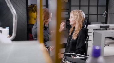 profesyonel makyaj ustası fırçalar kullanarak sarışın kadın güzellik Studio, dudaklarından ruj uyguluyor, modeli gülümsüyor