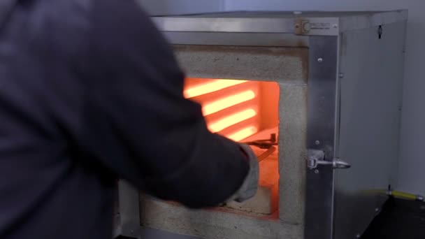 Arbeiter holt mit großer Zange glühendes Metallteil aus Ofen, Industrieanlage. — Stockvideo