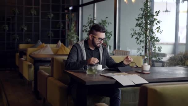 Красивый уверенный мужчина сидит в кафе и с чашкой зеленого чая . — стоковое видео