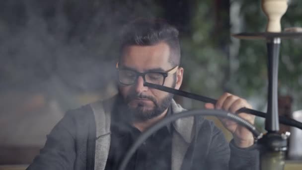 Close-up shot of a stylish adult guy smoking hookah indoor of a cafe alone. — Stock Video