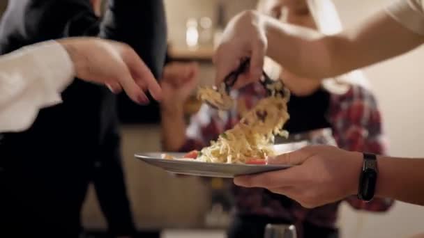Primer plano de amigos que se divierten cocinando para la fiesta, poniendo la comida en un plato juntos, un ingrediente cada uno . — Vídeos de Stock