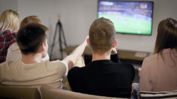 Мальчик смотрит футбольный матч по телевизору с девочками, друзья проводят время вместе в помещении . — стоковое видео