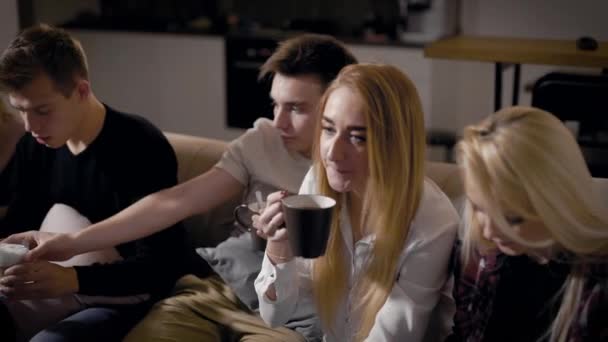 Moderna tonåringar sitter i vardagsrummet, dricka och titta på tv, mysiga homeparty. — Stockvideo