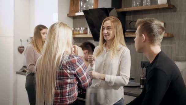 Estudantes alegres do sexo feminino e masculino estão conversando em uma cozinha durante a festa em casa, sorrindo e rindo — Vídeo de Stock