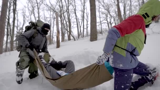 Caminhantes estão carregando mulher com a perna quebrada no palanquim na floresta, pisando sobre snowdrifts — Vídeo de Stock