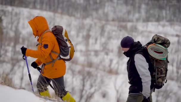 Människor som vandrar upp en sluttning täckt med gräs och snö — Stockvideo