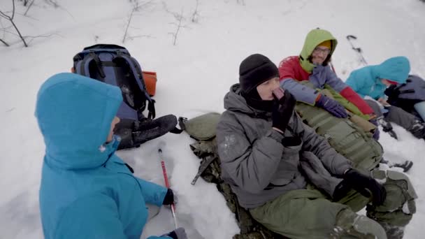 Quattro persone riposano durante il trekking invernale nella foresta, distese sulla neve e controllando gli zaini — Video Stock