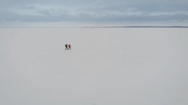 Doğada yürüyüş süren iki adamın havadan görünümü. Kalın kar tabakası ile kaplı donmuş nehir.