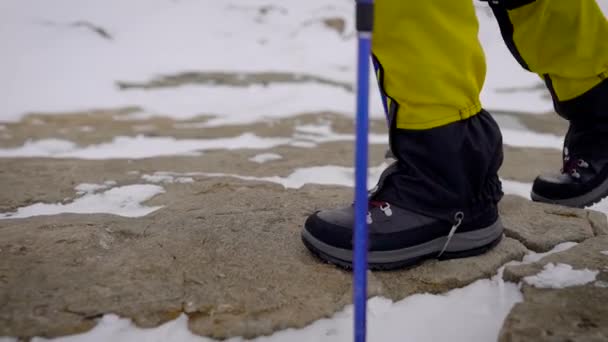 Close-up tiro de um caminhante pernas em botas pesadas e caminhantes polainas andando na neve e rochas em uma caminhada . — Vídeo de Stock