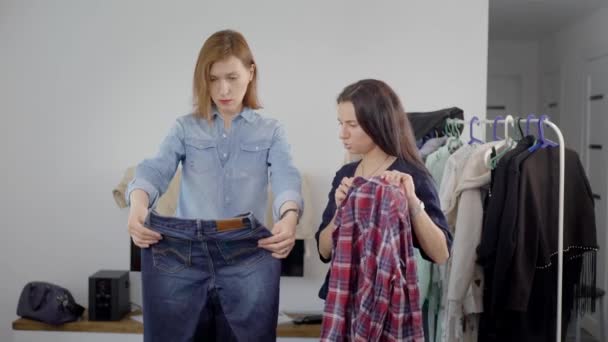 Δύο γυναίκες φιλενάδα αποσυναρμολογήσει ντουλάπα. Τα κορίτσια δοκιμάσουν διαφορετικά ρούχα και να αποφασίσουν πώς να ντύνονται. — Αρχείο Βίντεο