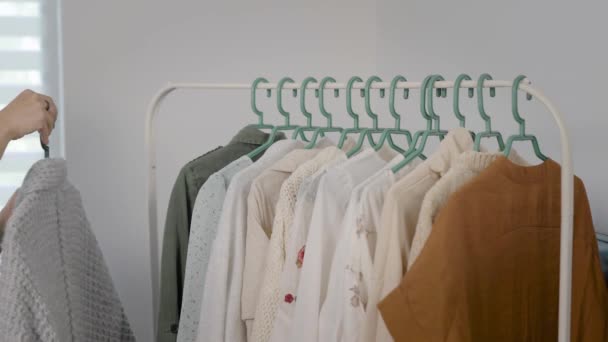 In het frame van de handen van een vrouw, gaan door kleding. Kleren hangen op een hanger, jurken, shirts, blouses enzovoort. Garderobe — Stockvideo