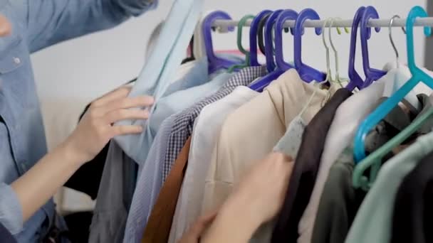 In het frame van de handen van een vrouw, gaan door kleding. Kleren hangen op een hanger, jurken, shirts, blouses enzovoort. Garderobe — Stockvideo