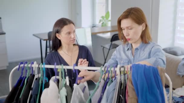 Två kvinnor flickvän demontera garderob. Flickor prova på olika kläder och bestämma hur man ska klä upp. — Stockvideo