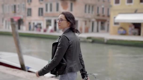 Egy gyönyörű lány egy bőr kabát sétál olaszul Velencében. Nő turista boldog róla vakáció Európában. — Stock videók