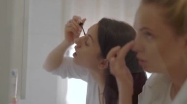 Sabah ayna nın önünde duran ve makyaj uygulayan iki genç kadının kapalı çekim.