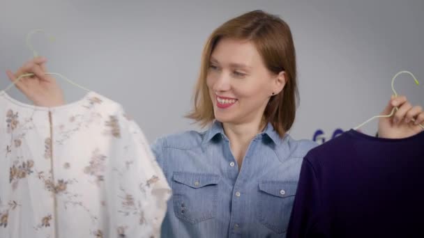 Portrait of a young woman at home. The girl holds the clothes in her hands and looks at the camera with a smile. — Stock Video