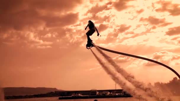 Flyboarding, egy új szélsőséges típusú tevékenység. Két flyboarders naplementekor, repülnek át a tó. Nyári szélsőséges. A sportolók sziluettjei az ég ellen. — Stock videók