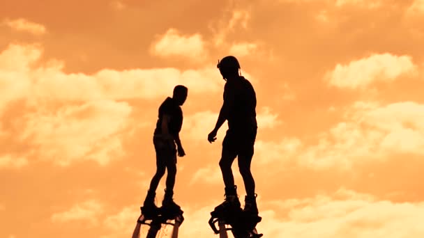 Flyboarding, egy új szélsőséges típusú tevékenység. Két flyboarders naplementekor, repülnek át a tó. Nyári szélsőséges. A sportolók sziluettjei az ég ellen. — Stock videók