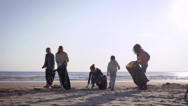 Las niñas voluntarias limpian la costa de la basura. Las mujeres apilan la basura lavada en bolsas negras. Acción voluntaria ecológica . — Vídeos de Stock