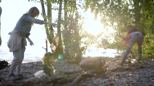 Mujeres atractivas están limpiando la costa de la basura. Voluntarios recogen residuos domésticos en bolsas de plástico negro . — Vídeos de Stock